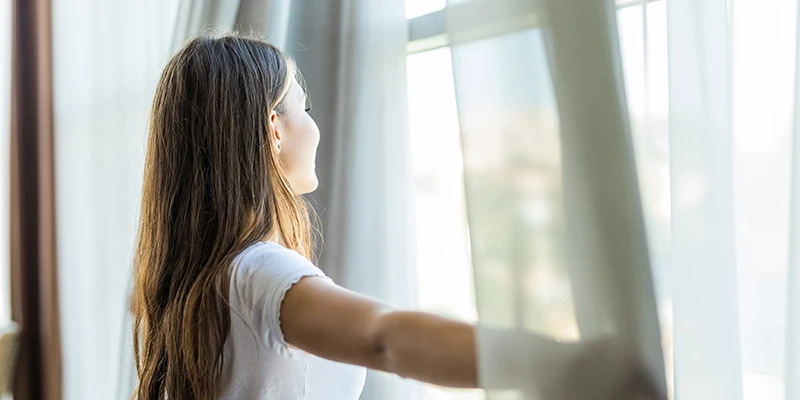 Mujer abriendo la ventana para ventilar la casa